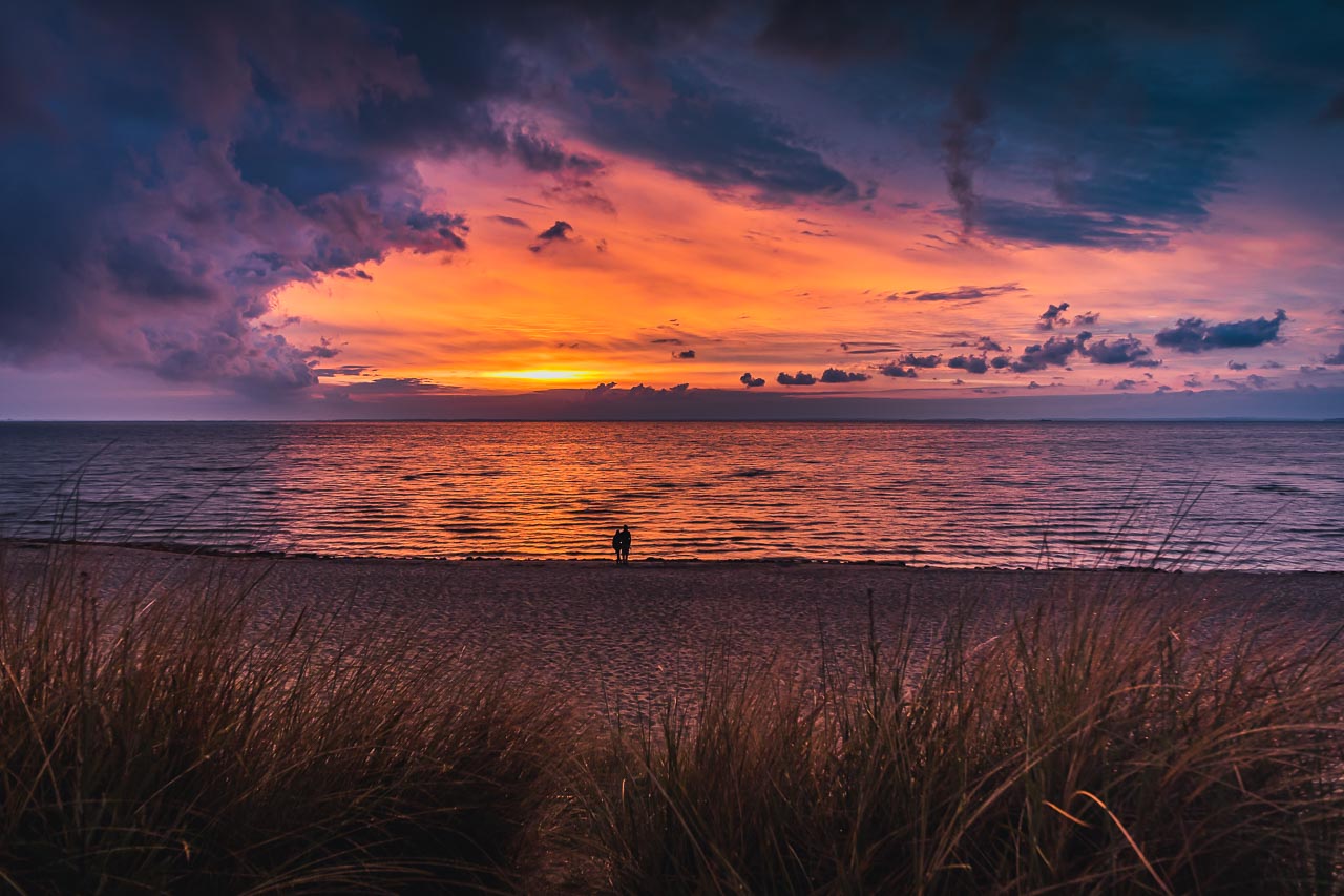 2 Menschen schauen sich den Sonnenuntergang am Strand Lubmins an