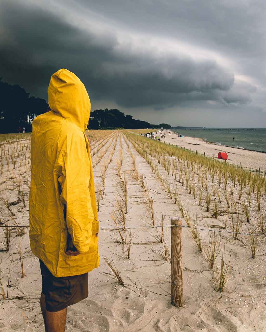 Mensch in gelber Regenjacke vor einer Schlechtwetterfront am Strand von Lubmin